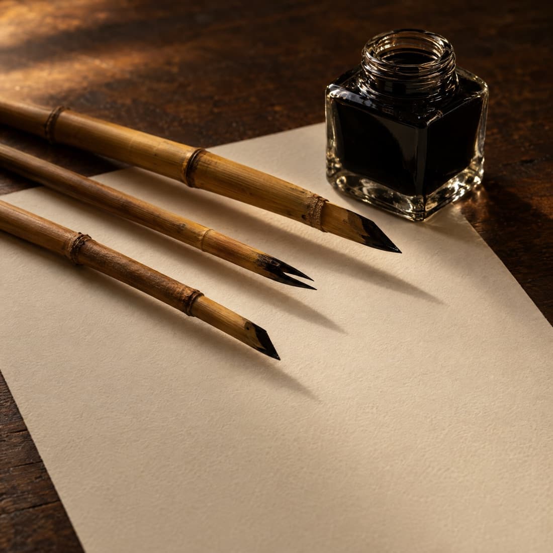 Drie rietpennen en een inktpotje op een blanco vel papier